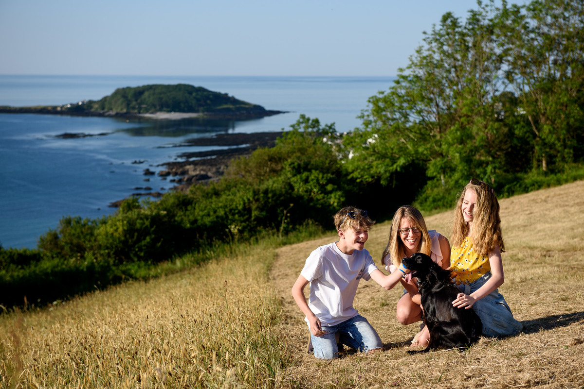 family-portrait-of-a-mother-with-her-two-children-playing-with-their-dog-in-a-field-overlooking-the-cornish-coast