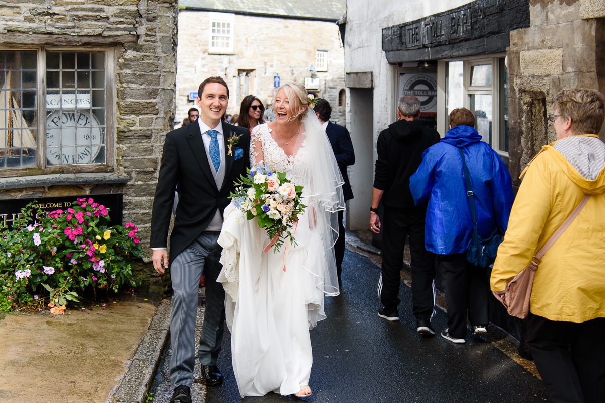 Bride and groom laughing as they walk through the crowded streets of Fowey