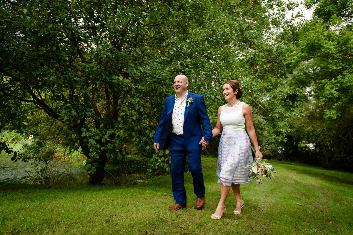 groom-and-bride-smiling-walking-hands-among-the-trees-at-The-Green-Cornwall
