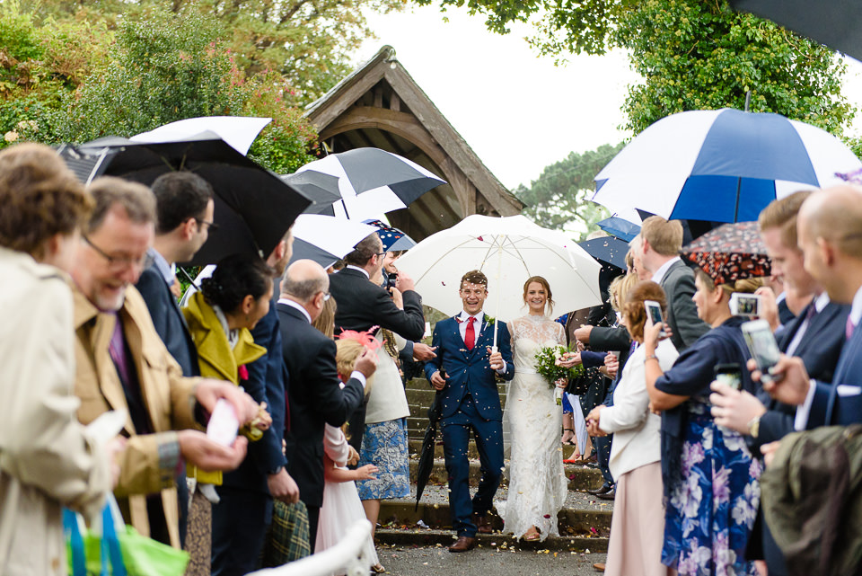 Bride and groom walk through tunnel of confetti and umbrellas